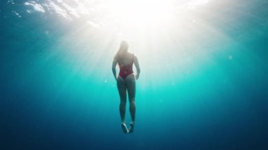 Teen girl in red suit dives and swims confidently underwater in the crystal clear tropical sea. Extreme slow motion footage