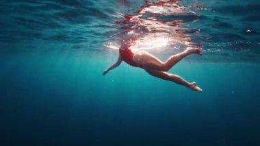 Kırmızı elbiseli genç kız gün batımında berrak tropikal denizde yüzer.