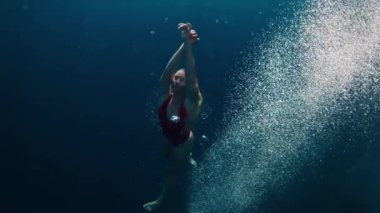 Kırmızı elbiseli genç kız kristal berrak tropikal denizde güvenli bir şekilde suya atlıyor ve yüzüyor. Aşırı yavaş çekim görüntüsü