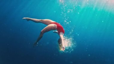 Kırmızı elbiseli genç kız denizde suyun altında yüzüyor. Rahat genç kız suya dalıyor ve yüzüyor. Kız suyun altında dans ediyor.