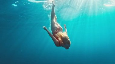 Kırmızı elbiseli genç kız suya atlıyor ve denizde yüzüyor. Rahat genç kız suyun altında süzülüyor. Kırmızılı kız suyun altında dans ediyor.