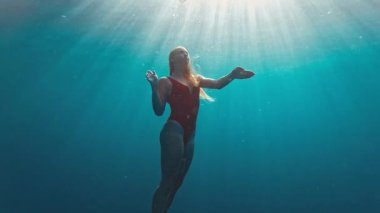 Kırmızı elbiseli genç kız denizde suyun altında yüzüyor. Rahat genç kız suya dalıyor ve yüzüyor. Kız suyun altında dans ediyor.