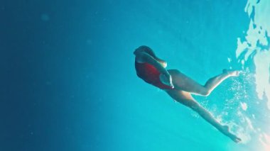 Kırmızı elbiseli genç kız suya atlıyor ve denizde yüzüyor. Rahat genç kız suyun altında süzülüyor. Kırmızılı kız suyun altında dans ediyor.