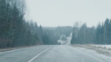 Kış yolu FPV. Kar fırtınası sırasında karla kaplı asfalt yolda kamera hareket ediyor..