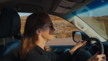 Genç kadın engebeli asfaltsız bir yolda büyük 4x4 'lük arabayı sürüyor.