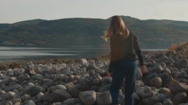 Genç kadın yürüyüşçü kayalık sahilde yürüyor.