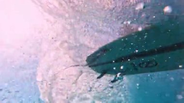 HIMMAFUSHI, MALDIVES - 25 Ekim 2024: Sörfçü temiz ve şeffaf suyla sualtı perspektifinden bir dalga sürüyor. Maldivler