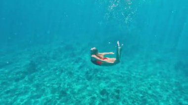 Kırmızı mayo giymiş profesyonel bir yüzücü mavi sularda zarafetle ilerler. Maldivler