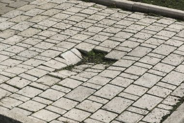 Background old cracked paving slabs with green grass between the tiles. Background of abandonment and decay of the urban structure. Old abandoned road surface