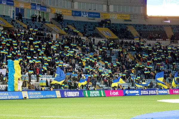 Odessa, Ukraine - Nov. 2021: Ukrainian football fans in stands of stadium with Ukrainian flags and national attributes enthusiastically support their national team. Football fans in stands of stadium