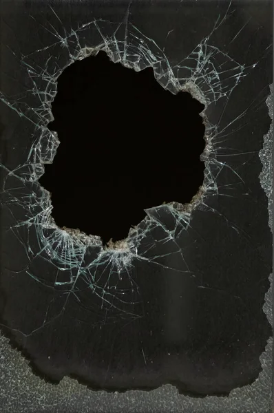 a bullet hole in glass is a real bullet hole of a large caliber projectile bullet. Glass door pierced by a bullet during the war, terrorist attack. Broken glass with cracks and a large hole in glass