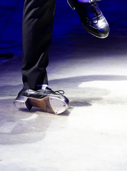 Men's legs in motion in stage trousers with stripes and leather shoes for Irish dancing on the floor. Black work boots for tap dancing with reflection on floor. selective focus. Step on stage close-up