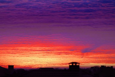 Gün batımında ya da gündoğumunda bulutlu güzel renkli dramatik gökyüzü. Yazlık köydeki yerleşim yerlerinin siluetlerinin üzerinde parlak renkli bir gün batımı. Gün batımının parlak renklerinde güzel bir manzara.