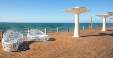 Modern beyaz rattan mobilyalar deniz kenarında oturma odasında bir açık havuz oluşturmak için. Plajda beyaz, modaya uygun güneş pansiyonları olan lüks yüzme havuzu. Manzara, lüks tatiller için iç mekan.