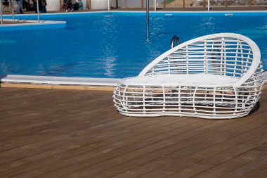 Modern beyaz rattan mobilyalar deniz kenarında oturma odasında bir açık havuz oluşturmak için. Plajda beyaz, modaya uygun güneş pansiyonları olan lüks yüzme havuzu. Manzara, lüks tatiller için iç mekan.