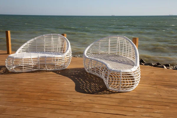 Modern white rattan furniture to create an outdoor pool in living room by sea. Luxurious swimming pool with white fashionable sun loungers on the beach. Landscape, interior for luxury holidays