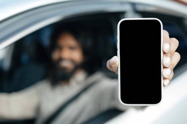 Gözlüklü gülümseyen genç Hintli adamın yakın çekimi. Büyük cep telefonlu, beyaz ekranlı, yeni lüks bir arabanın sürücü koltuğunda oturan, elinde bir alet olan büyük, boş ekran görüntüsü.