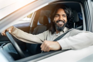 Neşeli genç bir adam bir arabada oturuyor, sıcak güneş ışığı altında, rahat bir atmosferi somutlaştıran, gündelik bir sürüş yaparken ışıl ışıl gülümsüyor..