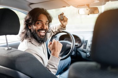 Uzun saçlı neşeli bir genç adam, anahtarlarını tutarken heyecanlanıyor ve bir arabanın şoför koltuğundaki başarısını kutluyor..