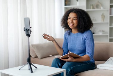 Modern Bloger. Siyah Kadın Etkilenen Vlog 'u için video kaydediyor, üç ayak üstünde akıllı telefon kullanan gülümseyen, kamerada konuşan ve hareket eden genç Afrikalı Amerikalı kadın,. 