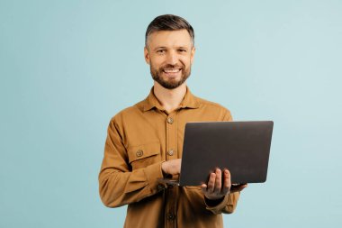 Çevrimiçi iş için dizüstü bilgisayar kullanan neşeli orta yaşlı bir adam ya da mavi stüdyo geçmişi ile iletişim kuran. Yüksek kalite fotoğraf