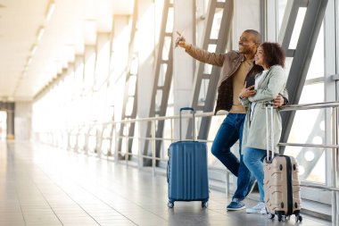 Pasaportları ve biletleri olan genç Afrikalı bir çift havaalanında bekliyor ve uzaklaşıyorlar mutlu Afrikalı erkek ve kadın birlikte seyahat ediyorlar terminaldeki uçuş kapısını kontrol ediyorlar,. 