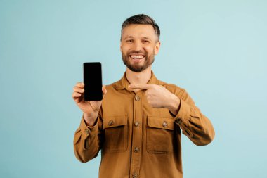 Güzel cep telefonu teklifi. Heyecanlı Avrupalı orta yaşlı adam akıllı telefonu işaret ediyor, yeni uygulamaya duygusal tepki veriyor, mavi arka planda tek başına duruyor, stüdyo çekimi. Yüksek kalite fotoğraf