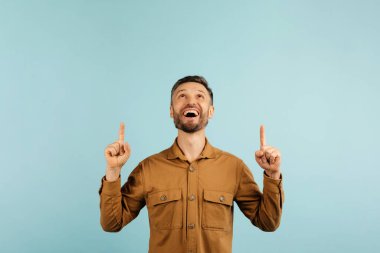 Heyecanlı, yakışıklı, gri saçlı, orta yaşlı, orta yaşlı bir adam başının üstündeki fotokopi odasına bakıyor, mavi arka planda izole edilmiş, güzel bir teklif sunuyor. Yüksek kalite fotoğraf