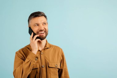 Akıllı telefonuyla konuşan orta yaşlı bir adamın portresi, fotokopi odasına bakıyor, mavi stüdyo arka planında duruyor, afiş, panorama. İletişim, telefon görüşmesi kavramı. Yüksek kalite fotoğraf