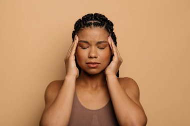 Bin yıllık mutsuz Afro-Amerikan kadın acı çekiyor şakak ovuyor, baş ağrısı çekiyor, bej arka planda izole edilmiş, yakın plan çekimi var. Yüksek kalite fotoğraf