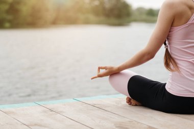Huzurlu bir göl kenarında oturan bir kadın yoga yapıyor. Güneş ışıl ışıl parlıyor. Huzurlu duruşunu aydınlatıyor. Ve yakınlardaki sakin suyu..