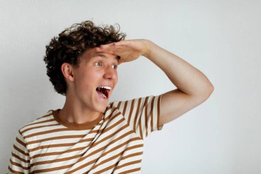 Kıvırcık saçlı neşeli bir genç adam şen şakrak gözlerini kısıyor ve sanki uzaktan bir şey arıyormuş gibi elini alnına kaldırıyor. Sıradan çizgili bir gömlek giyiyor..