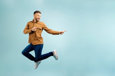 Duygusal Orta yaşlı bir adam mavi stüdyo arkaplanındaki fotokopi odasına atlıyor. Mutlu adam iyi bir teklif sunuyor. Reklam için boş yer gösteriyor, panorama. Yüksek kalite fotoğraf