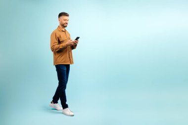 İletişim için mobil uygulama. Mavi stüdyo arka planında izole edilmiş akıllı telefonu kullanan neşeli orta yaşlı adam arkadaşlarına mesaj atıyor, kaydırıyor, kopyalayabiliyor. Yüksek kalite fotoğraf