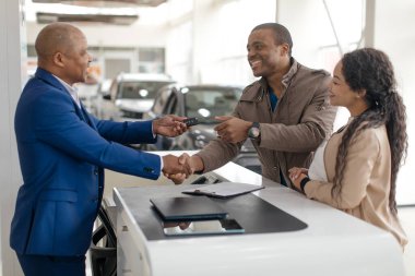 Satıcı, Oto galerisinde ayakta duran Afrikalı Neşeli Alıcılara Yeni Araba Anahtarı Veriyor. Aile Arabası Satın Alma. Seçici Odaklanma. Yüksek kalite fotoğraf