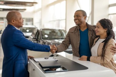 Araba almak. Afrikalı çiftler araba satış merkezinde satış elemanları ve imza dağıtan kağıtlarla el sıkışıyor. Seçici Odaklanma. Yüksek kalite fotoğraf
