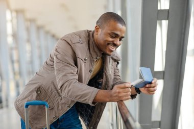 Havaalanında bekleyen bavullu Afrikalı bir gencin portresi, Terminal 'de beklerken pasaportu elinde tutan yakışıklı bir Afrikalı Amerikalı. Yüksek kalite fotoğraf