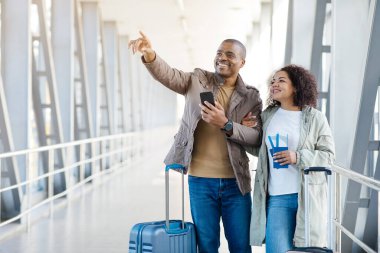 Seyahat teklifi. Mutlu Afro-Amerikan Turistler, parmak kaldıran çift dışarıda havalimanında duran bavulla Yön Gösterme pozu veriyor. Tatil Turu Reklam Konsepti. Yüksek kalite fotoğraf