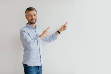 Neşeli bir adam, parlak ve minimalist bir odada dururken coşkuyla el kol hareketi yapar. Boş bir duvarı işaret ederek dikkatleri görünmeyen bir elemente ya da fikre çekiyor..