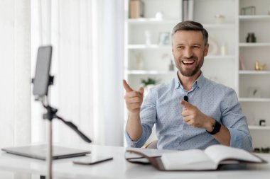 Gülümseyen bir adam, ışık ve kitaplarla çevrili iyi organize edilmiş masasındaki sanal bir tartışma sırasında coşkuyla jest yapar ve canlı bir atmosfer yaratır..