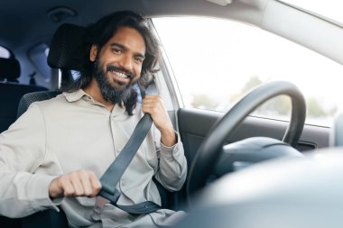 Sürücü koltuğunda oturan neşeli bir adam emniyet kemerini bağlar ve yolculuğuna başlamaya hazırdır. Güneş ışığı arabanın camlarından içeri akarak sıcak bir ortam yaratıyor..