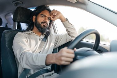 Genç bir adam düşünceli bir şekilde araba sürer, güneşli bir günün tadını çıkarırken düşüncelerini yansıtırken bakışları ileriye odaklanır. Arabanın içi iyi aydınlatılmış..