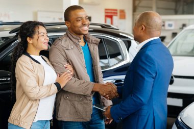 Genç bir Afro-Amerikalı çift bir araba galerisinden araç alımını sonuçlandırıyor. Satıcıyla el sıkışırken galeride sözleşmeyi birlikte gözden geçiriyorlar..