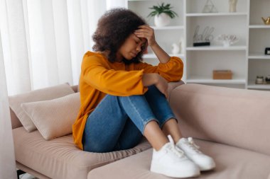 Depresyondaki genç siyahi kadın baş ağrısından muzdarip, alnını ekşiterek bastırıyor, Afro-Amerikan bayan kaşlarını çatıyor, evde stres veya şiddetli migren belirtileri gösteriyor.