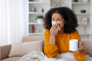 Soğuk ve soğuk algınlığı. Hasta siyah kadın burnunu kağıt mendile sümkürdü ve evde çay içti. Hasta Afro-Amerikan kadın, oturma odasında kanepede oturmuş kendini kötü hissediyordu.