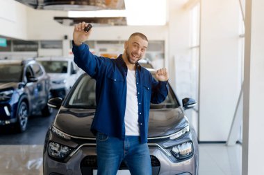 Büyük bir otomobil galerisinde arabanın önünde duran mutlu adam, otomobilin anahtarını gösteriyor ve kameraya gülümsüyor, milenyum adamı galeri merkezinde yeni bir araca sahip oluyor,