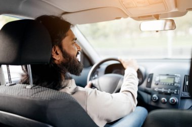 Hintli bir adamın araba sürüşünün arka görüntüsü, odaklanmış bir şekilde ileriye bakan, ellerini direksiyonda tutan, arabasıyla gezmekten zevk alan, omuz manzaralı,