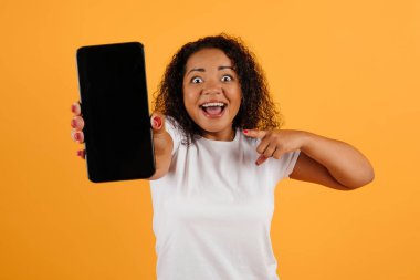 Elinde boş ekranla Smartphone 'u işaret eden heyecanlı siyahi kadın, cep telefonu uygulama tasarımınız için kopyalama alanı gösteren neşeli Afrikalı Amerikalı kadın, sarı arka planda duruyor,