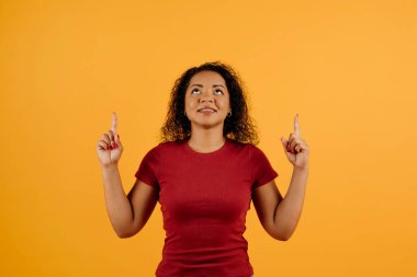 Genç Afrikalı Amerikalı bir kadın, iki eliyle fotokopi alanını işaret ediyor. Siyahi bir kadın, merakla ve ilgiyle yukarı bakıyor. Sarı stüdyo arka planında tek başına duruyor.