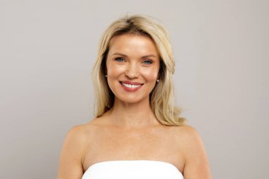 Gülümseyen orta yaşlı sarışın kadın portresi düz saçlı, çekici olgun kadın mutlu görünüyor, açık gri stüdyo arka planında duruyor fotokopi alanı ile